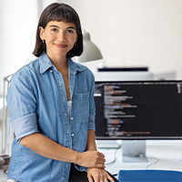A young woman, a software developer, smiling at the camera with lines of code displayed on her computer screen.
